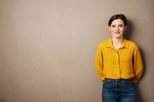 young smiling business woman with yellow blouse stands in front of brown background