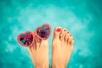 Rolgordijnen Womens feet with red pedicure against blue water background © Sunny studio