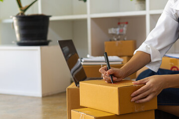 Asians working with laptop computers checking numbers online, selling start-ups, small business owners, e-commerce concepts, young women pack items into boxes to ship to customers.