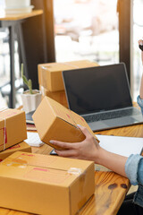 Asians working with laptop computers checking numbers online, selling start-ups, small business owners, e-commerce concepts, young women pack items into boxes to ship to customers.