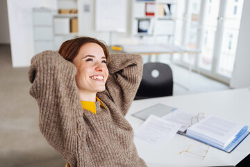 young modern business woman sits at desk and looks up relaxed