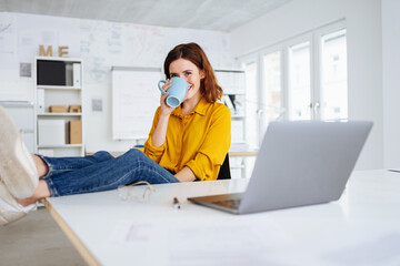 young modern business woman takes break in office and drinks her cup of coffee