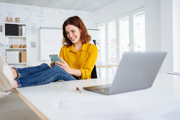 young modern business woman sitting relaxed at her desk and looking at her cell phone in the office