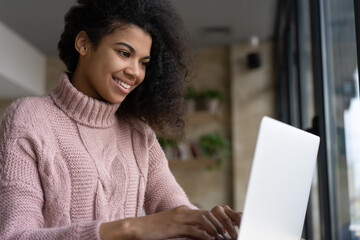 Beautiful smiling African American woman using laptop computer communication online sitting at workplace. Successful freelancer copywriter typing working from home. Student studying, online education 