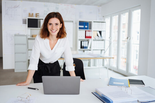 young laughing woman stands at desk in office and looks into camera
