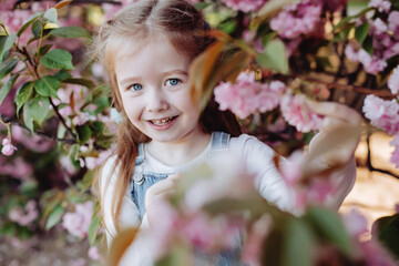 Fototapeta premium Close up of beautiful red-haired girl sincerely smiling in the park near sakura.