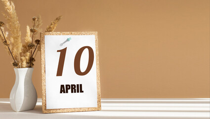 April 10. 10th day of month, calendar date.White vase with dead wood next to cork board with numbers. White-beige background with striped shadow. Concept of day of year, time planner, spring month