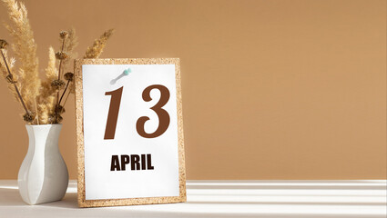 April 13. 13th day of month, calendar date.White vase with dead wood next to cork board with numbers. White-beige background with striped shadow. Concept of day of year, time planner, spring month