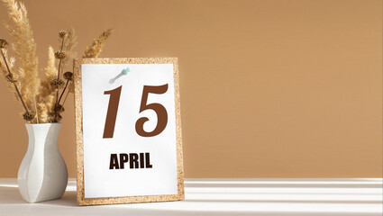 April 15. 15th day of month, calendar date.White vase with dead wood next to cork board with numbers. White-beige background with striped shadow. Concept of day of year, time planner, spring month