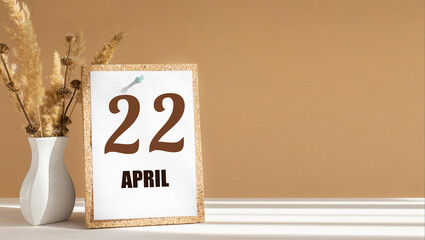 April 22. 22th day of month, calendar date.White vase with dead wood next to cork board with numbers. White-beige background with striped shadow. Concept of day of year, time planner, spring month