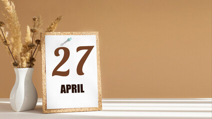 April 27. 27th day of month, calendar date.White vase with dead wood next to cork board with numbers. White-beige background with striped shadow. Concept of day of year, time planner, spring month