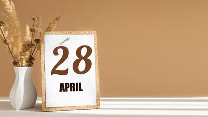 April 28. 28th day of month, calendar date.White vase with dead wood next to cork board with numbers. White-beige background with striped shadow. Concept of day of year, time planner, spring month