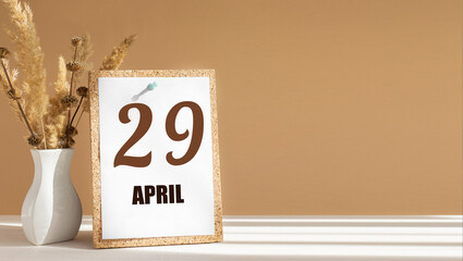 April 29. 29th day of month, calendar date.White vase with dead wood next to cork board with numbers. White-beige background with striped shadow. Concept of day of year, time planner, spring month