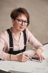 Positive mature Caucasian architectural designer in eyeglasses sitting at table and drawing line using ruler