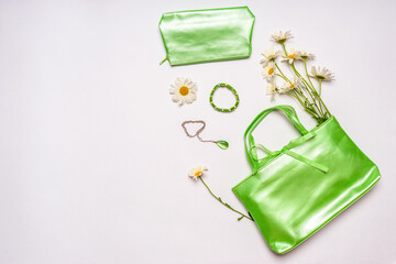 Stylish feminine handbag, cosmetic bag and jewellery with daisy flowers on white background. Female accessories in green pastel color. Spring or summer fashion concept. Flat lay, top view, copy space