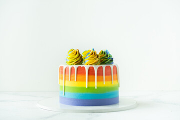 Rainbow cake with whipped cream top on the white background. Birthday cake with multicolored cream...