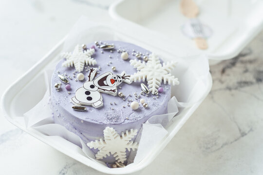 KYIV, UKRAINE - JANUARY 24: Frozen character on cake with blue cream cheese frosting decorated with snowflakes and Olaf snowman. Winter cake on white background. Korean trendy bento cake
