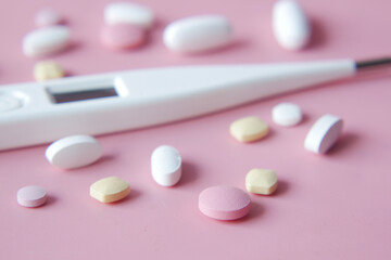  digital thermometer and medical pills on pink background 