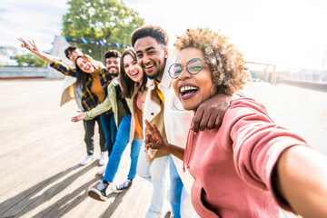 Multiracial friends group taking selfie pic with smartphone outside - Happy young people having fun walking on city street - Friendship concept with guys and girls enjoying summertime day outside - Powered by Adobe
