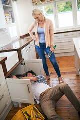 Honey, I think we should just call a professional. Shot of a man fixing pipes under his kitchen sink while his wife watches.