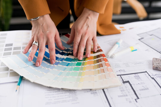 Close-up of architect woman choosing samples of wall paint. Interior designer looking at color swatch for creating project. House renovation, color palettes, architecture and interior design concept.