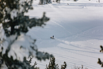 The snowmobile climbs up the slope of the mountain through an snow field