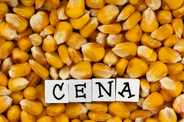 The wording "Cena" translated as "Price" composed on the background of bulk corn grain. High price of cereals. Scene lit by uniform, soft light.