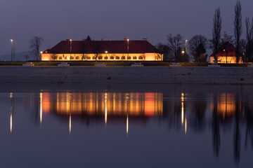 Fototapeta premium The illuminated building of the City Assembly in Slavonski Brod is reflected in the water of the Sava River at night in Croatia
