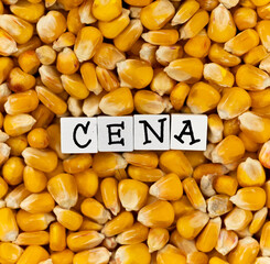 The wording "Cena" translated as "Price" composed on the background of bulk corn grain. High price of cereals. Scene lit by uniform, soft light.