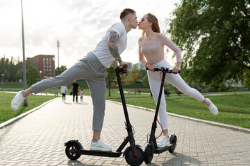 Fototapeta na wymiar Young couple on vacation having fun driving electric scooter through the park