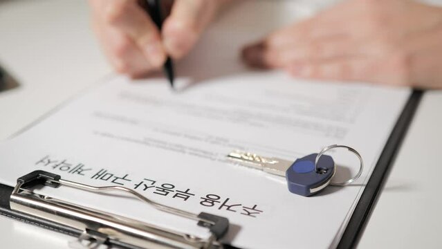 real estate purchase and sale agreement in Korean-speaking. Female or male hand signs the deal documents. Realtor's office. The deal took place, dollars and the key to the house or apartment.