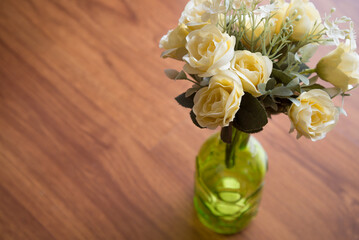 Artificial rose flower in bottle jar with beautiful sunlight at home on wooden table background. Lifestyle and home decoration concept.
