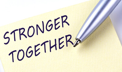 Sticky Note Message STRONGER TOGETHER with pen on the white background