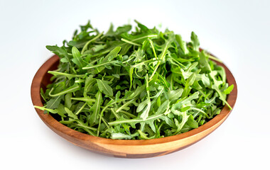 Fresh arugula leaves in wooden bowl on a white background