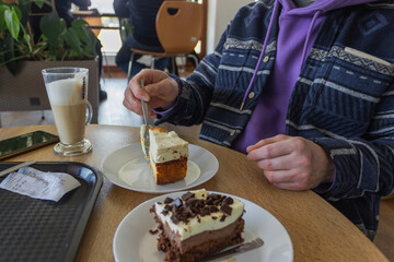 Man's hand holds a fork for eating cheesecake. Man having coffee break with latte in the cafe.