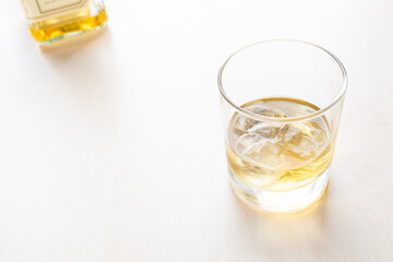 whiskey on the rocks in glass and bottle on background on pale table with copyspace