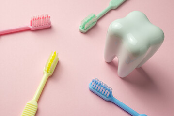 White tooth and colorful toothbrush on pink background, dental care concept.