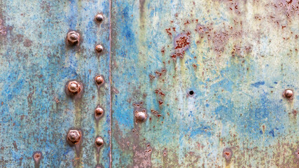 Grunge industrial background of worn metal with faced blue paint and rust spots joined by rivets...