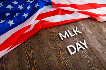 the word MLK day laid with silver metal letters on wooden surface with crumpled USA flag at upper side