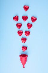 Concept of female menstruation. Red menstrual cup with red hearts imitating menstrual bleeding. Conceptual photo.