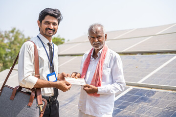 Village farmer receiving check from banker in front of solar panel - concept of financial support...