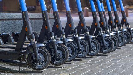 Electric scooters waiting at the curb ready to be rented and driven away. Several blue e-scooters...