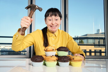 Frau mit gelber Bluse, sitzt im Büro und haut mit Hammer auf einen haufen Donats ein