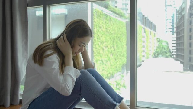 Depressed Asian woman sitting alone with cuddle herself and Loneliness sad female think grief trouble life problem in bedroom. Negative emotion and mental health concept, sitting alone at condo