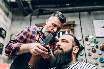 Fototapeta na wymiar The barber trims the beard of the customer with shaving machine.
