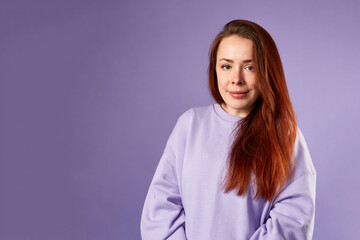 Caucasian woman in violet sweatshirt. Natural look. Smiling. long red hair. Violet background