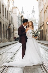 Naklejka premium An international wedding couple, a European bride and an Asian groom walk around the city together.