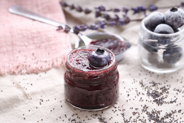 A glass jar with delicious blueberry jam with fresh berries, lavender and chia seeds on a light background. Healthy eating.