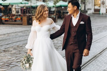 An international wedding couple, a European bride and an Asian groom walk around the city together.