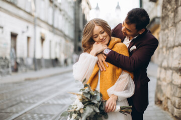 An international wedding couple, a European bride and an Asian groom walk around the city together.